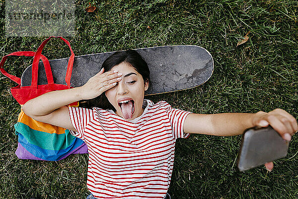 Junge Frau streckt die Zunge heraus  während sie ein Selfie mit ihrem Smartphone im Park macht