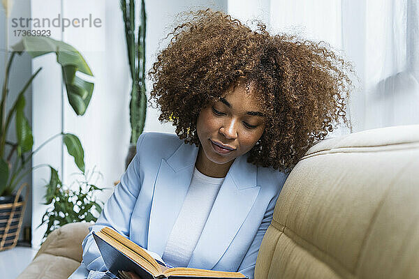 Junge Geschäftsfrau liest ein Buch  während sie auf dem Sofa im Wohnzimmer sitzt