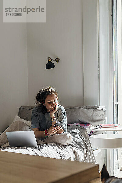 Frau benutzt Mobiltelefon  während sie auf dem Bett sitzt