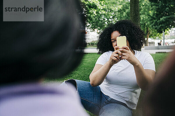 Junge Frau fotografiert Freunde mit dem Smartphone im Park