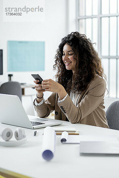 Lächelnde Geschäftsfrau mit Laptop und Smartphone am Schreibtisch