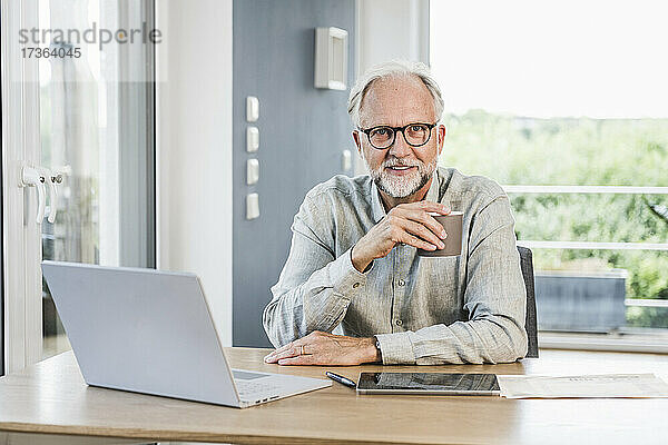Geschäftsmann mit Brille hält Tasse am Schreibtisch im Home Office