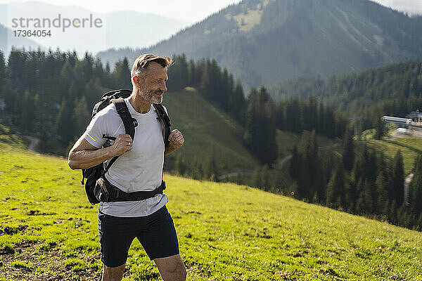 Lächelnder Mann mit Rucksack beim Wandern auf einem Berg