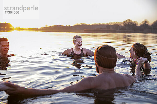 Frauen mit männlichen Freunden lachen  während sie sich im kalten Wasser am Morgen vergnügen