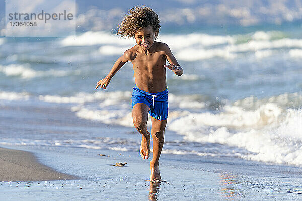 Fröhlicher Junge läuft an der Küste am Strand