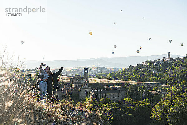 Spanien  Kastilien und Leon  Segovia  Zwei Schwestern machen ein Selfie mit fliegenden Heißluftballons und historischen Gebäuden der Stadt
