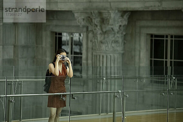 Weibliche Touristin fotografiert durch die Kamera  während sie an einem Glasgeländer steht