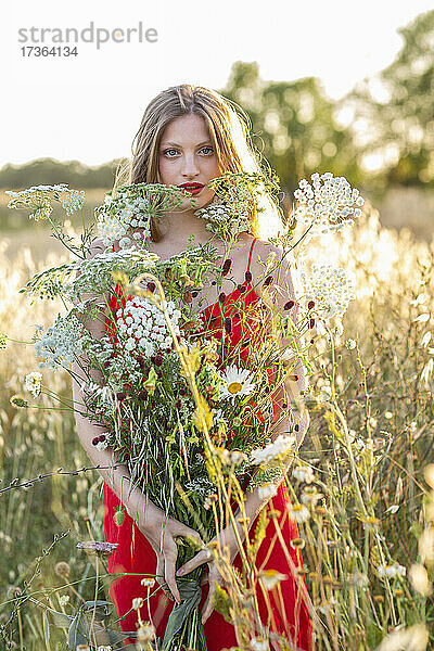 Blonde junge Frau hält Wildblumen in einem Feld