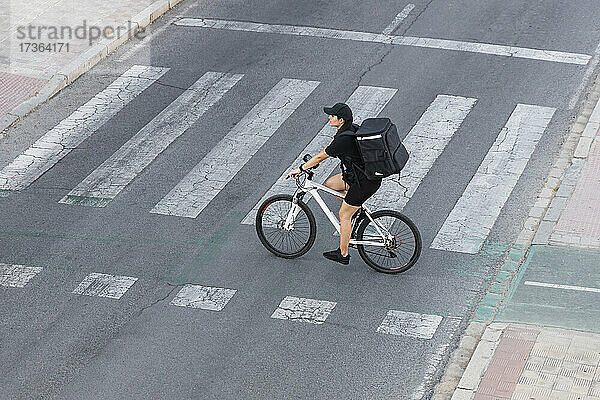 Weiblicher Zusteller mit Rucksack auf dem Fahrrad an einer Kreuzung