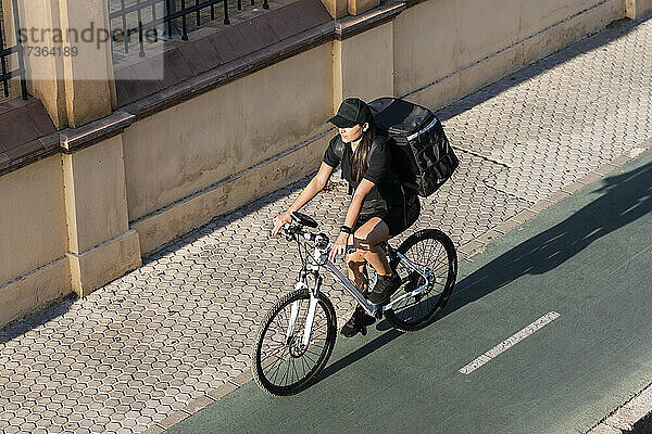 Weibliche Lieferperson fährt Fahrrad auf der Straße an einem sonnigen Tag