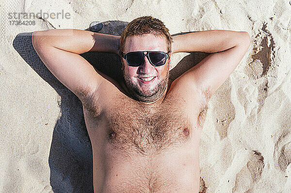 Lächelnder schwuler Mann  der sich an einem sonnigen Tag im Sand entspannt