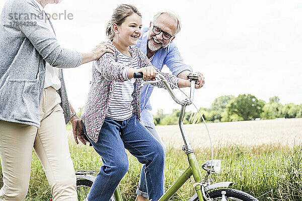 Enkelin übt mit Großeltern auf der Wiese Fahrradfahren