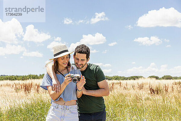 Frau mit Hut zeigt ihrem Freund die Kamera  während sie auf einer Wiese steht