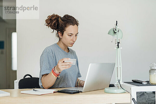 Berufstätige Frau mit Kreditkarte beim Online-Bezahlen mit dem Laptop zu Hause