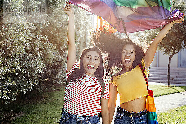 Sorglose lesbische Frauen winken bei Sonnenuntergang mit der Regenbogenflagge