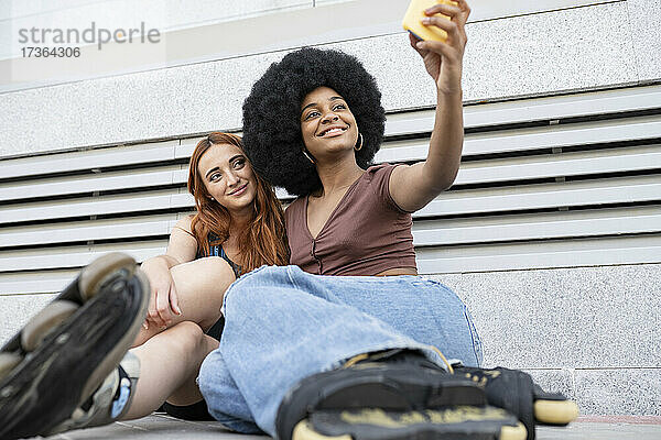 Lächelnde Afro-Frau  die ein Selfie mit einer Freundin vor einer Wand macht