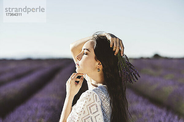 Junge Frau mit geschlossenen Augen in einem Lavendelfeld an einem sonnigen Tag