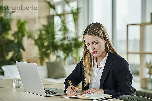 Weibliche Auszubildende schreibt in der Molkerei  während sie am Schreibtisch im Büro sitzt