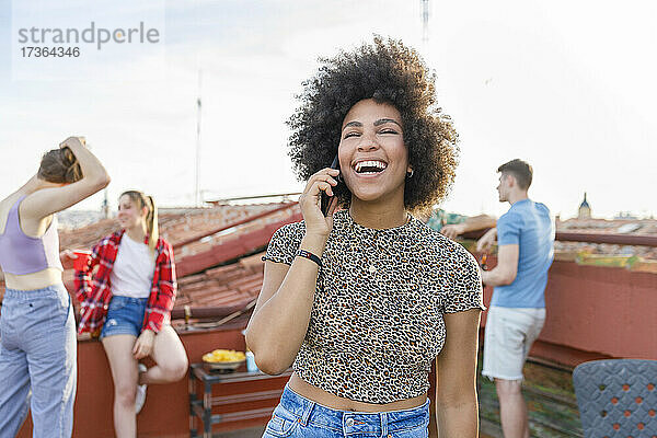 Junge Frau lacht  während sie in einer Party auf der Terrasse mit ihrem Smartphone telefoniert