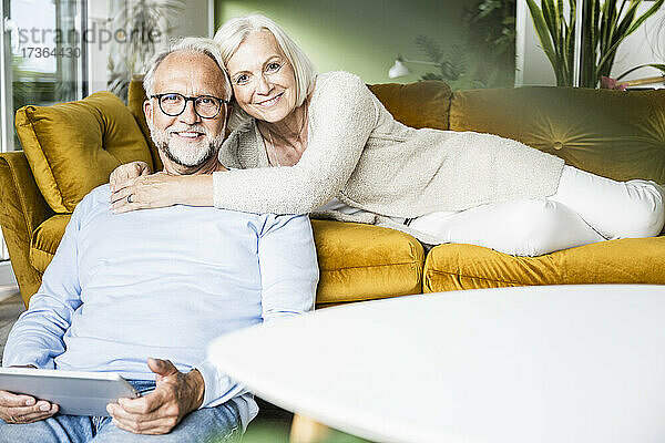 Lächelnde Frau  die einen Mann umarmt  während sie sich zu Hause auf dem Sofa ausruht