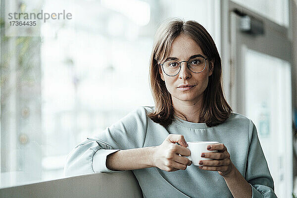 Junge Frau mit braunen Haaren hält eine Kaffeetasse  während sie in einem Café sitzt