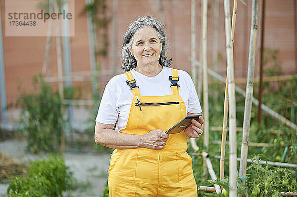 Lächelnde ältere Frau mit digitalem Tablet im Garten