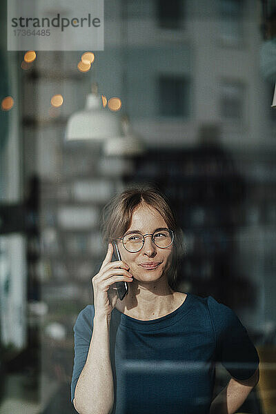 Junge Geschäftsfrau  die mit ihrem Handy telefoniert  gesehen durch ein Glasfenster