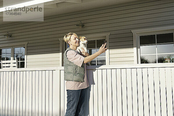 Frau macht Selfie über Smartphone mit Hund in der Nähe des Geländers vor dem Haus
