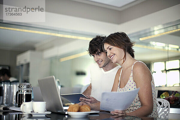 Lächelnde Frau mit Dokument  die ihren Laptop mit ihrem Freund zu Hause teilt