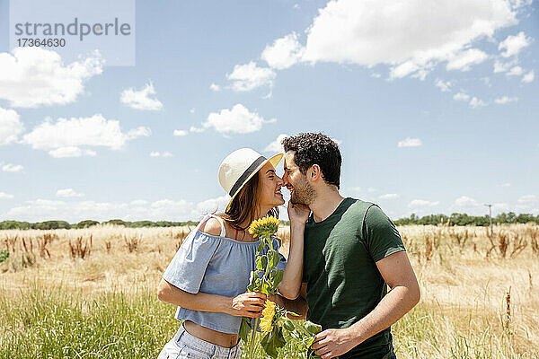 Lächelndes Paar mit Sonnenblumen  das sich an einem sonnigen Tag die Nasen reibt