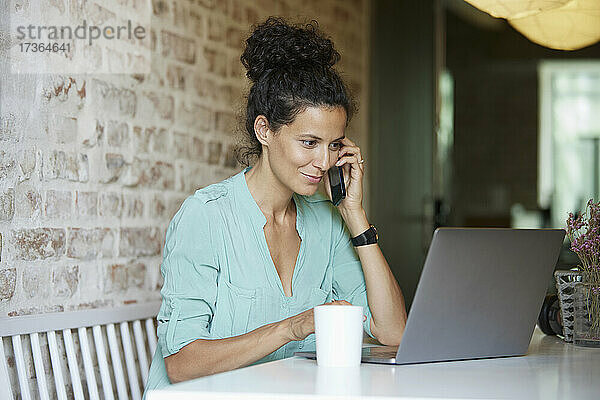 Weibliche Berufstätige  die am Arbeitsplatz mit dem Handy telefonieren und einen Laptop benutzen