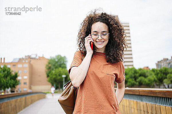 Schöne  lächelnde  lockige Frau mit Brille  die mit einem Mobiltelefon spricht