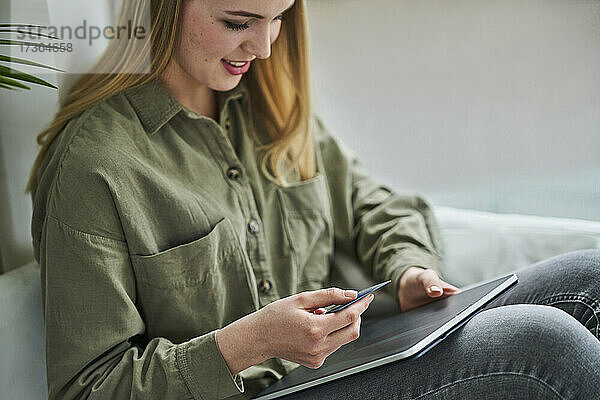Weibliche Auszubildende sitzt mit Kreditkarte und digitalem Tablet im Büro