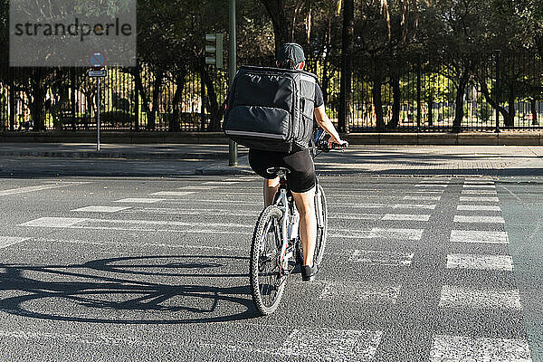 Junge Lieferfrau mit Rucksack auf dem Fahrrad auf der Straße an einem sonnigen Tag
