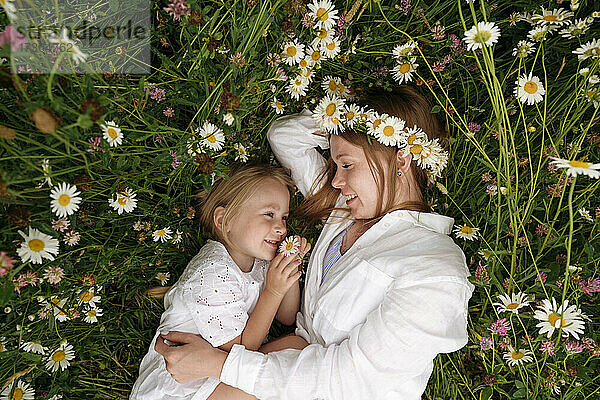 Lächelnde blonde Frau ruht sich mit ihrer Tochter inmitten von Kamillenpflanzen aus