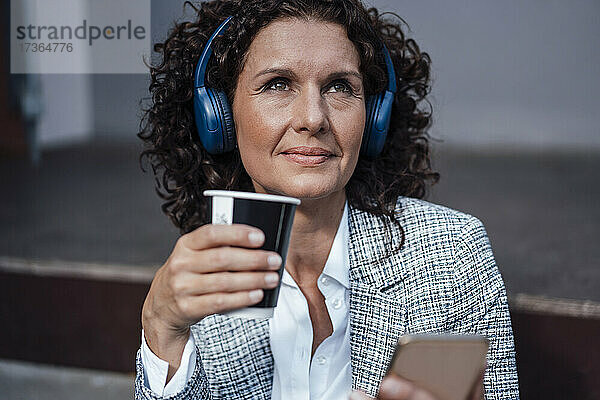 Reife Geschäftsfrau hört Musik und hält eine Kaffeetasse