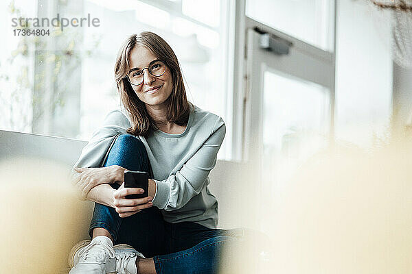 Lächelnde Frau sitzt mit Handy in einem Café