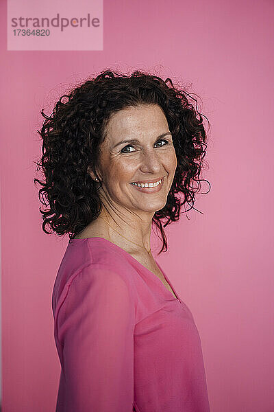 Lächelnde Geschäftsfrau stehend vor rosa Hintergrund