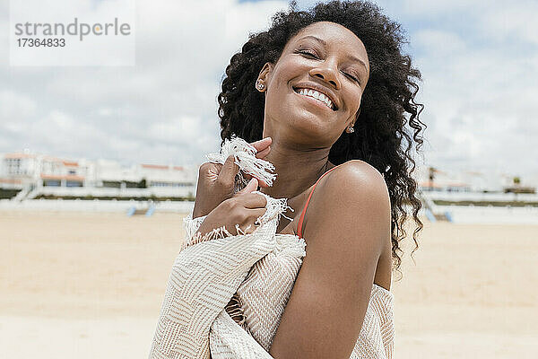 Lächelnde Frau mit geschlossenen Augen und Strandtuch an einem sonnigen Tag