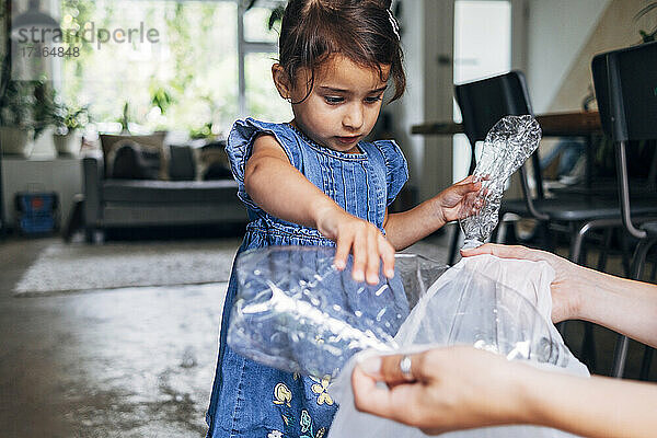 Mädchen hilft Tochter beim Sammeln von zerkleinerten Plastikflaschen im Müllsack zu Hause