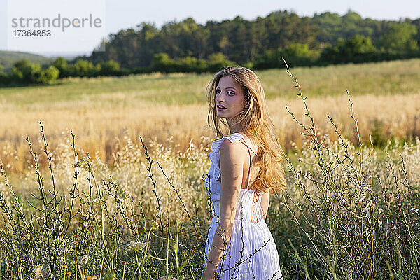 Schöne Frau in weißem Kleid steht inmitten von Pflanzen im Feld