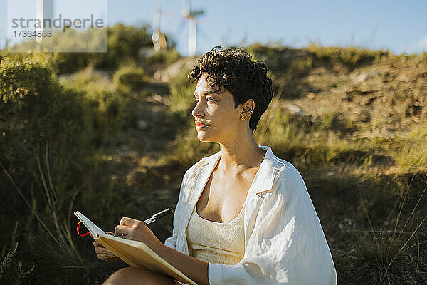 Nachdenkliche Frau sitzt mit Notizbuch an einem sonnigen Tag