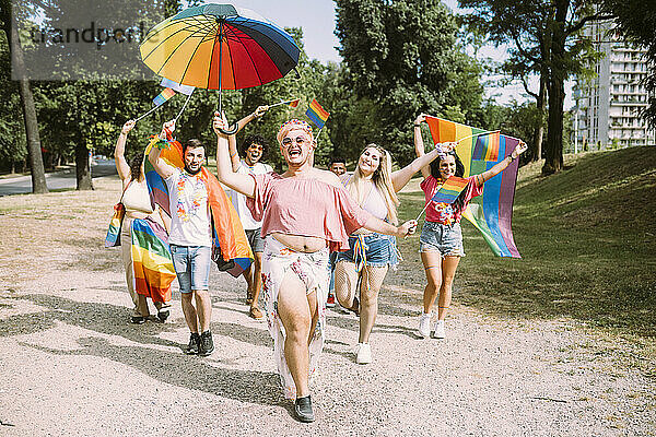 Glückliche männliche und weibliche Freunde mit Regenbogenfahnen  die im Park spazieren gehen