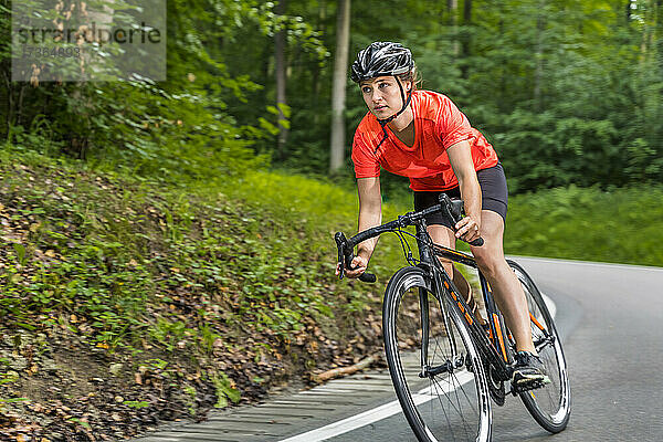 Weibliche Athletin fährt Fahrrad auf einer Straße im Wald