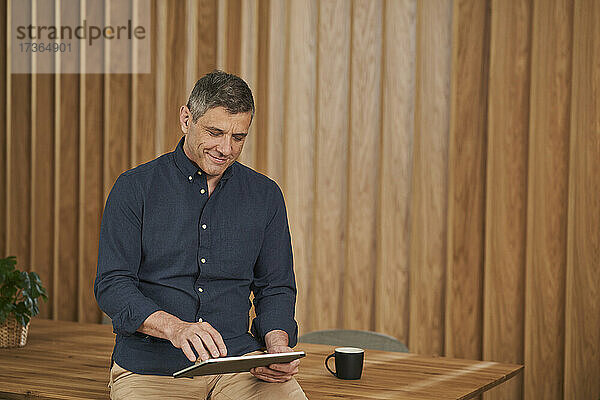 Lächelnder Geschäftsmann  der ein digitales Tablet benutzt  während er am Konferenztisch im Sitzungssaal sitzt