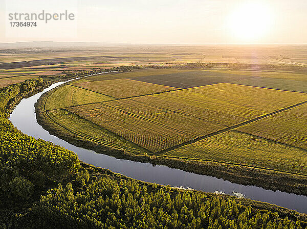 Luftaufnahme des Flusses und der weiten landwirtschaftlichen Felder im Sommer bei Sonnenuntergang