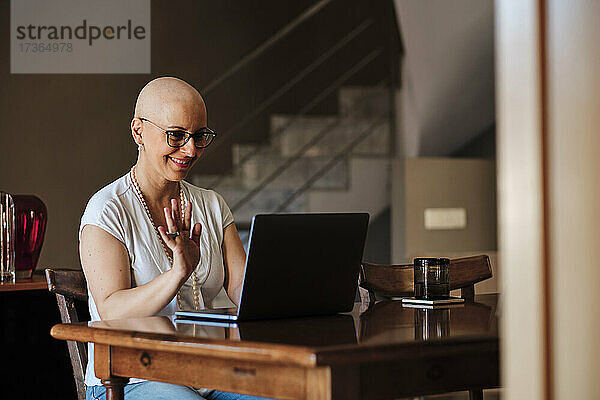 Lächelnde reife Frau winkt während eines Videogesprächs über einen Laptop zu Hause