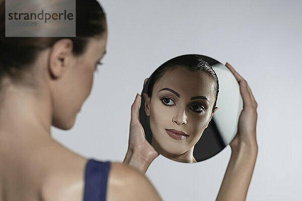 Frau schaut auf Spiegelbild vor weißem Hintergrund