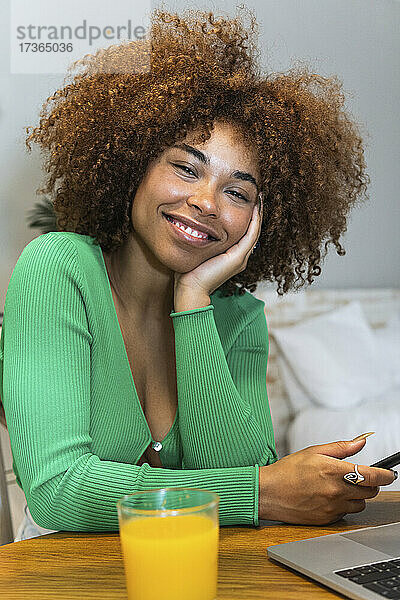 Junge Afro-Frau mit Hand am Kinn am Tisch im Home Office