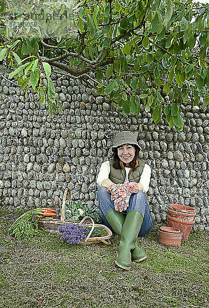 Lächelnde Frau mit Körben vor einer Mauer im Gemüsegarten sitzend